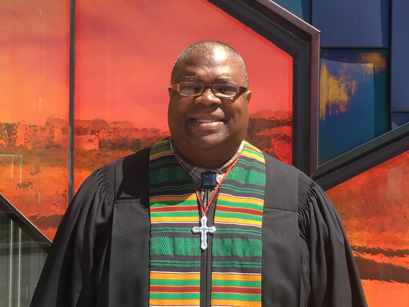 Pastor Mark McGhee Sr. smiling in front of orange and blue glass.